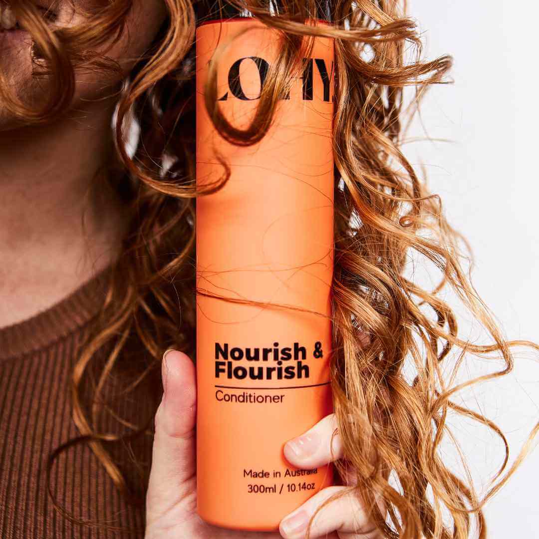Bottle of curly hair conditioner nestled in red hair curls