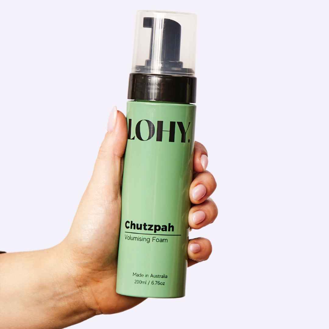 Hand holding a bottle of chutzpah volumizing mousse