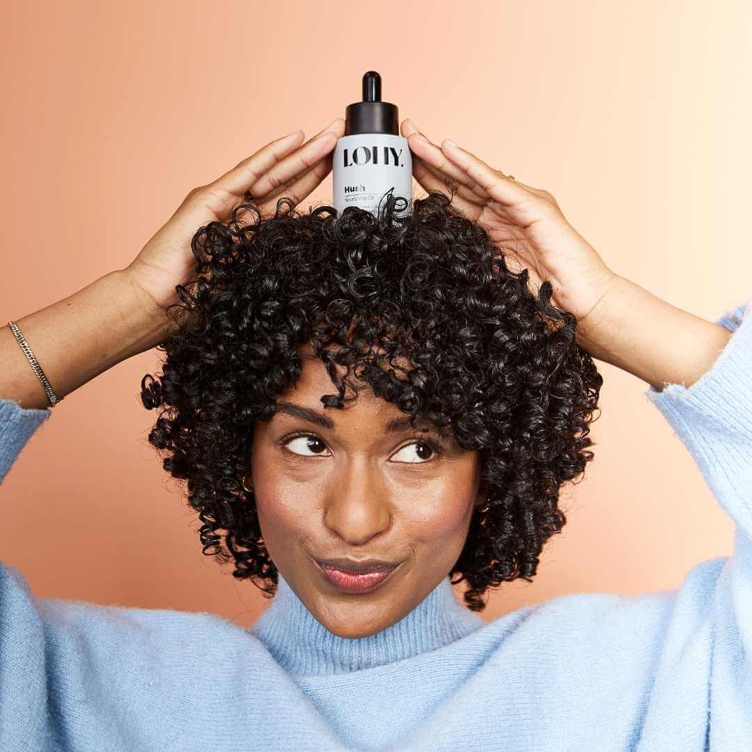 coily hair model holding bottle on head