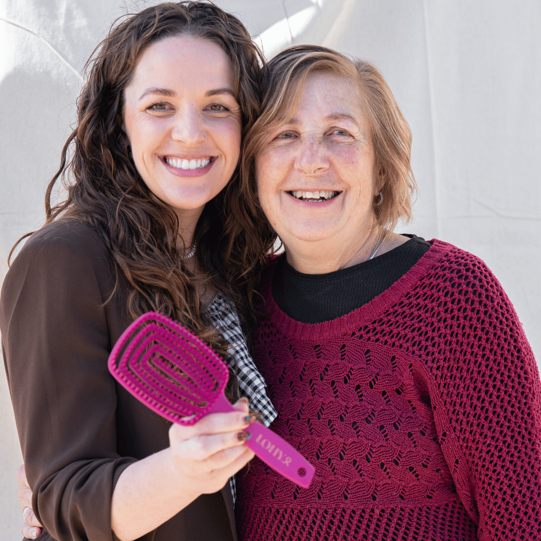 Jonina and her mum smiling and holding pink paddle brush